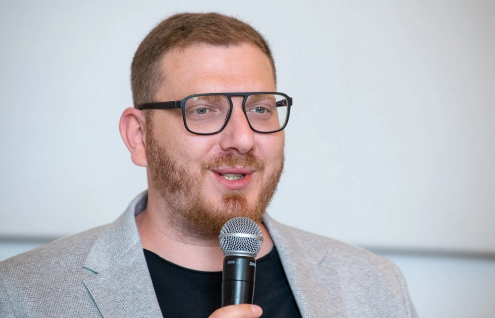 Лев Львовский, экономист и преподаватель BISEB, говорит в микрофон во время публичного выступления.